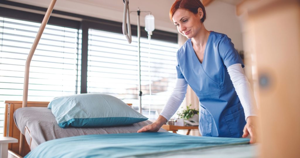Woman in scrubs making hospital bed