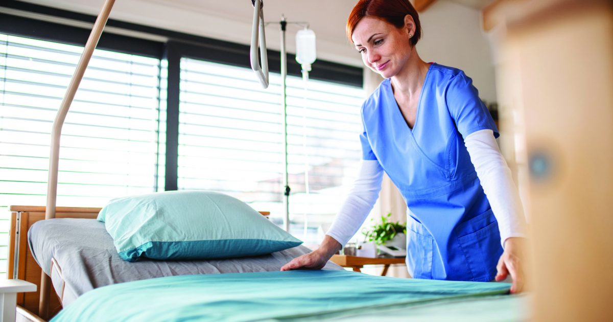 Portrait of female nurse or housekeeping staff changing sheets in hospital.